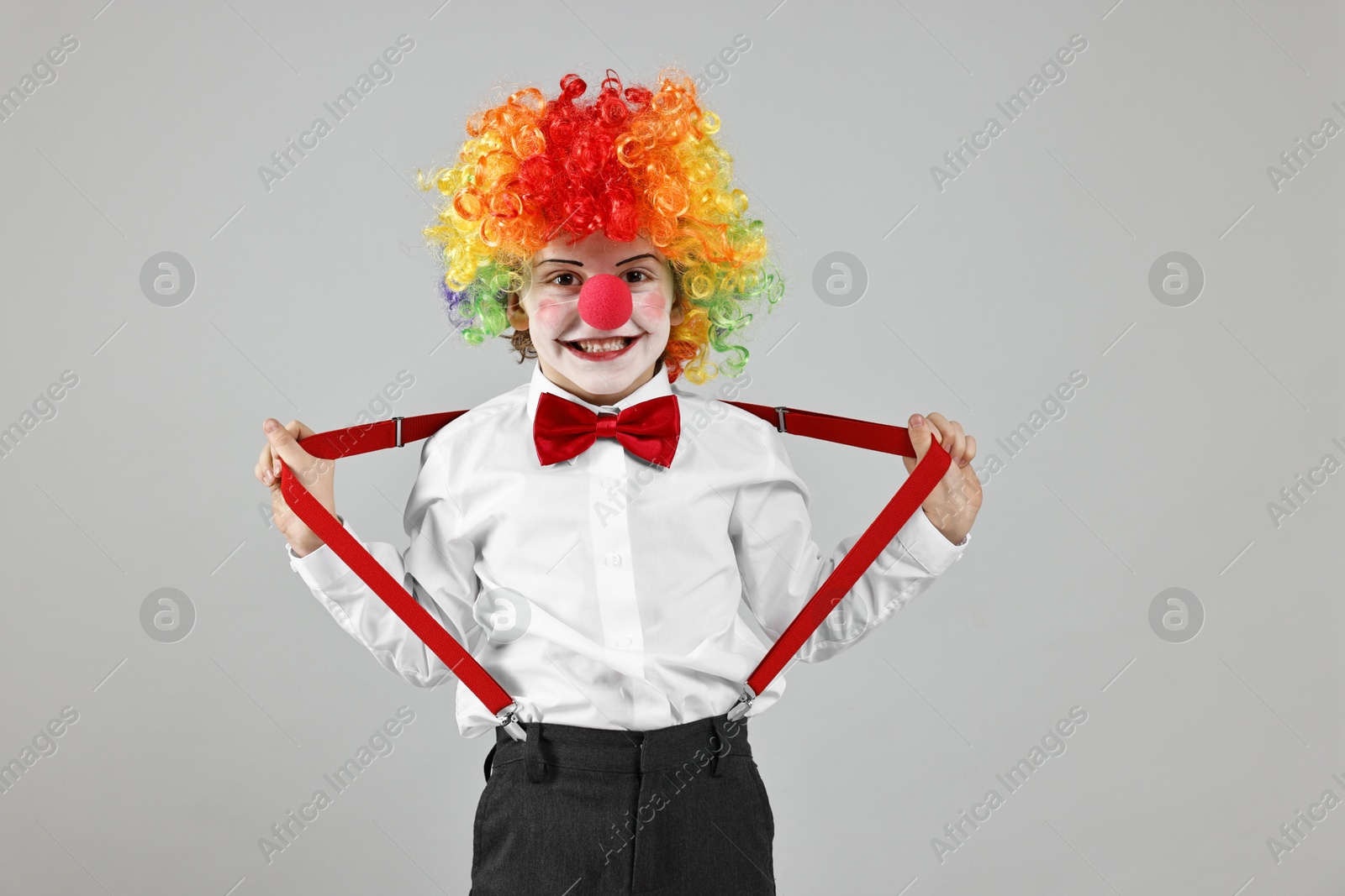 Photo of Happy little boy in clown wig and red nose on grey background. Surprise party