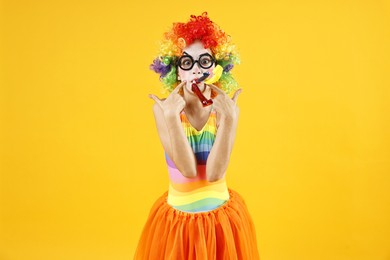 Photo of Girl dressed like clown pointing at blowers on yellow background. Surprise party