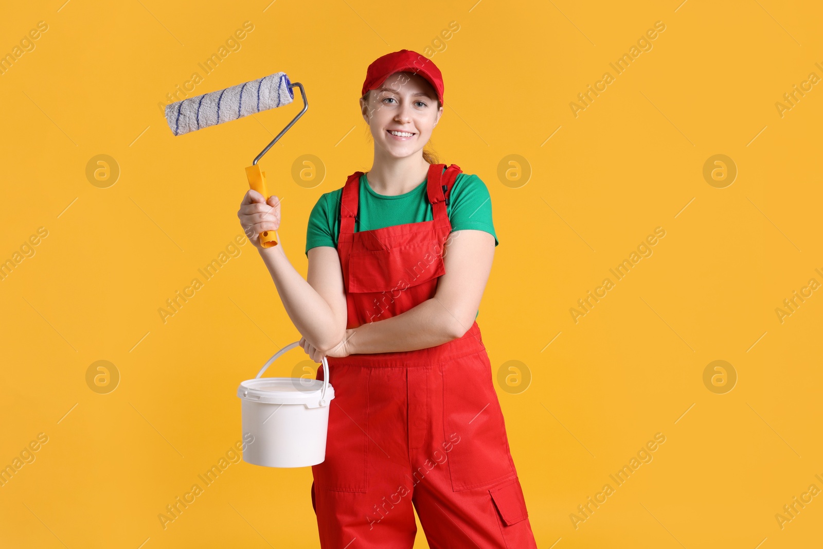 Photo of Professional painter with roller and bucket of paint on orange background