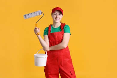 Photo of Professional painter with roller and bucket of paint on orange background