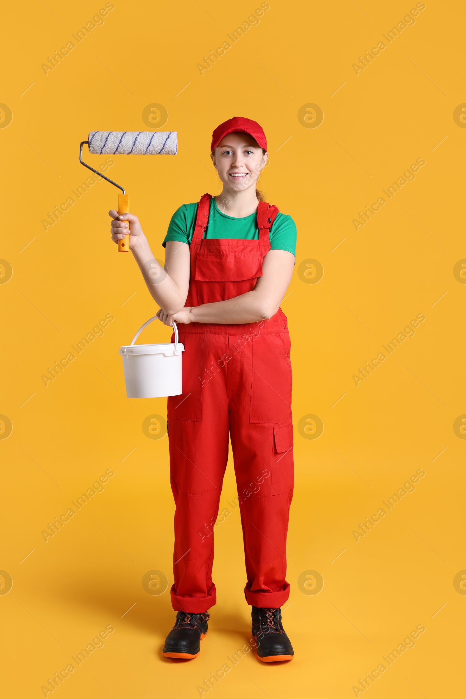 Photo of Professional painter with roller and bucket of paint on orange background