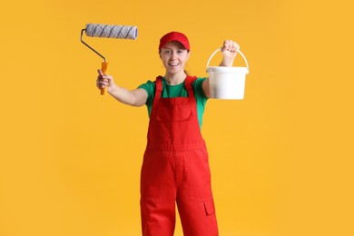 Photo of Professional painter with roller and bucket of paint on orange background