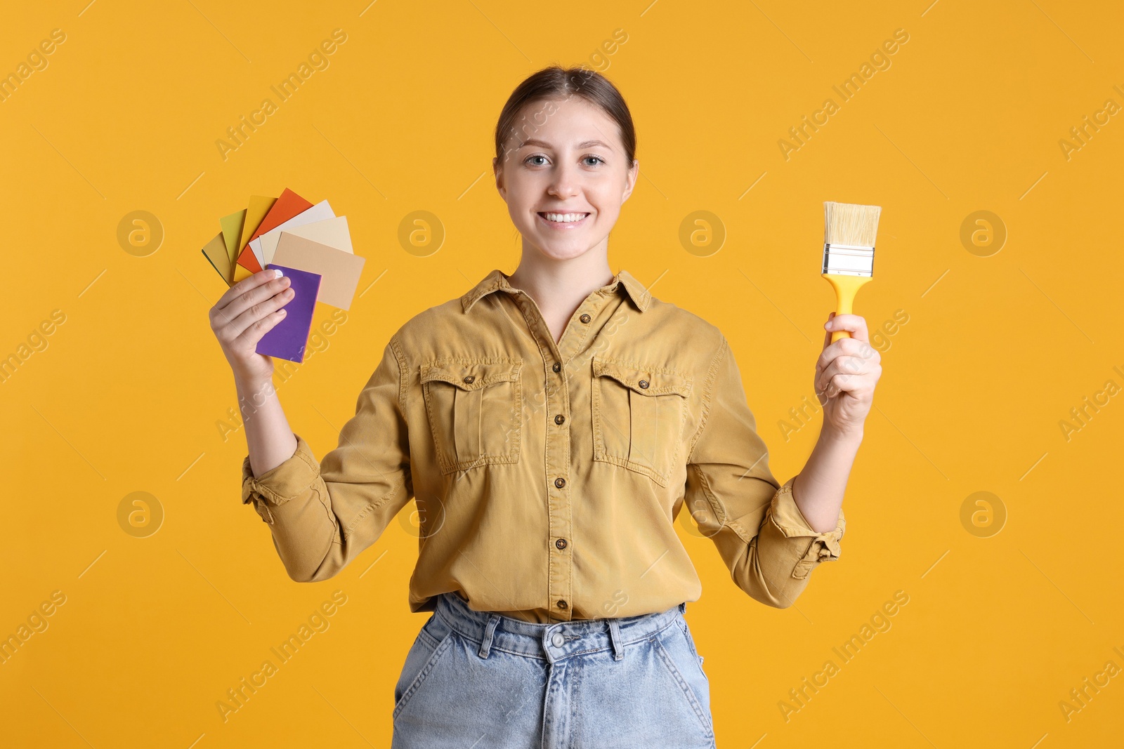 Photo of Woman with paintbrush and color samples on orange background