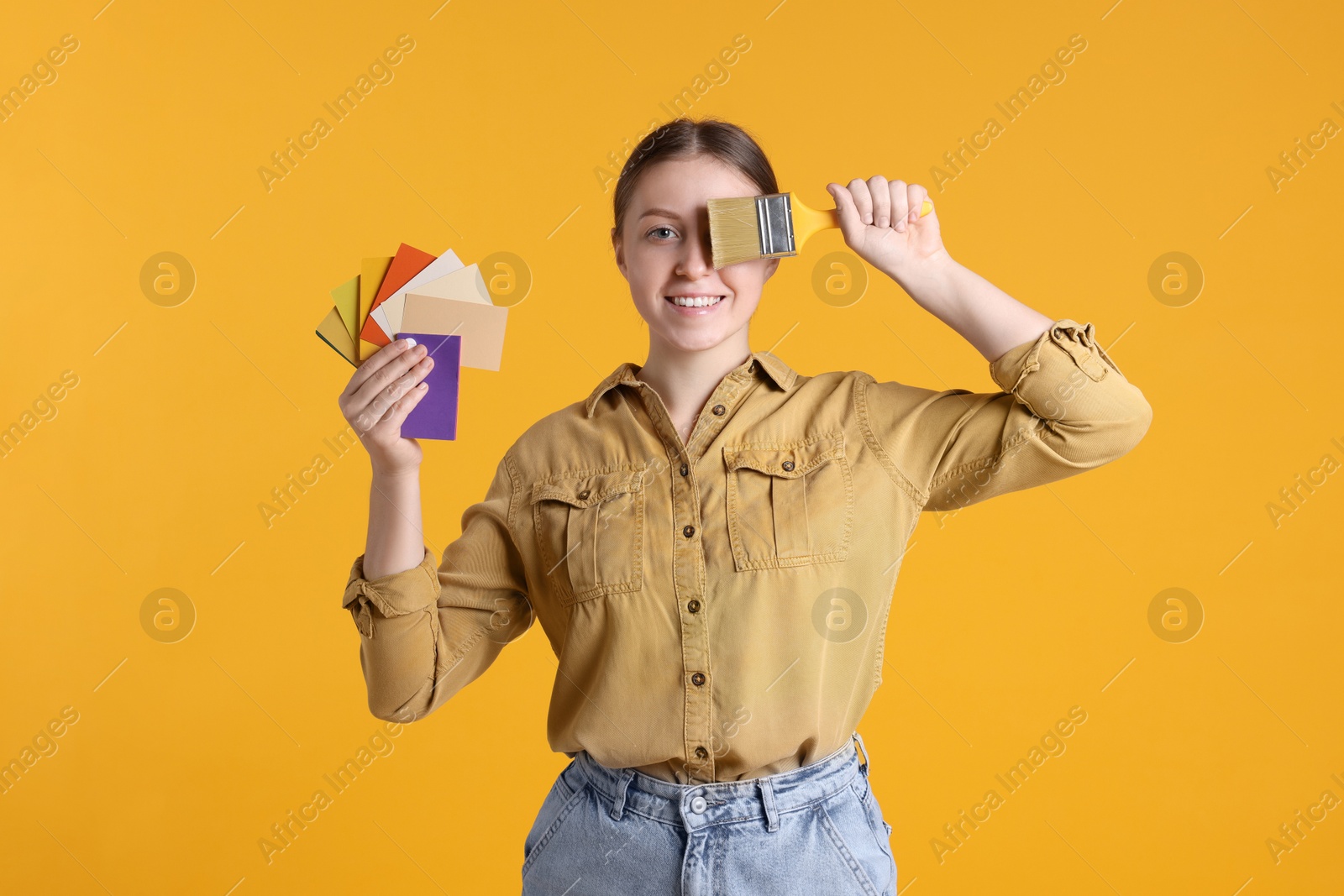 Photo of Woman with paintbrush and color samples on orange background