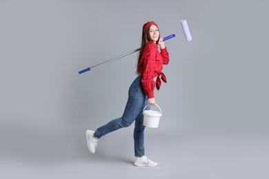 Photo of Woman with roller and bucket of paint on light grey background