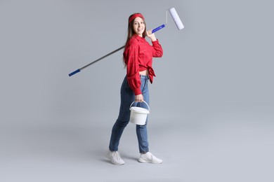 Photo of Woman with roller and bucket of paint on light grey background