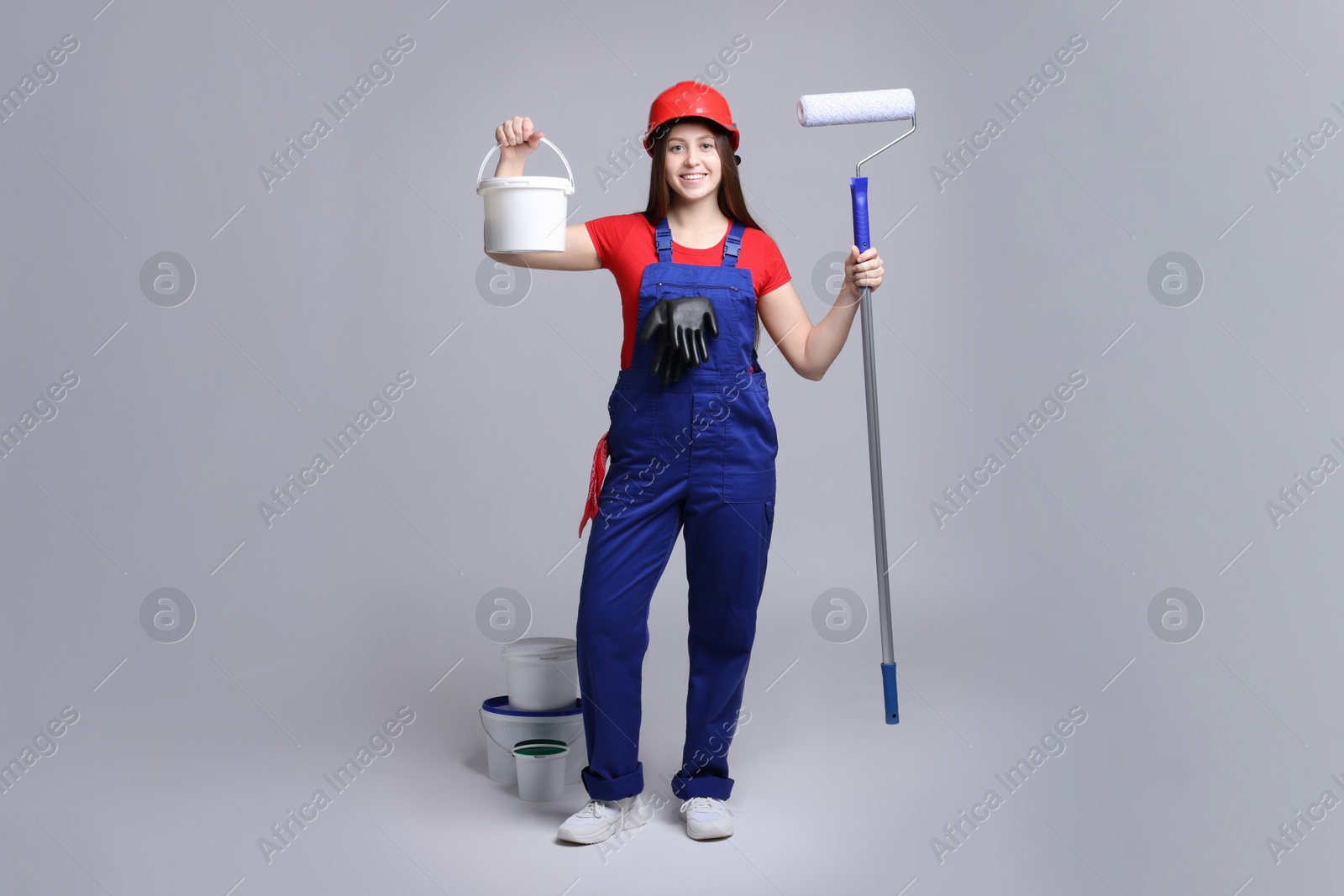 Photo of Professional painter with roller and buckets of paint on light grey background