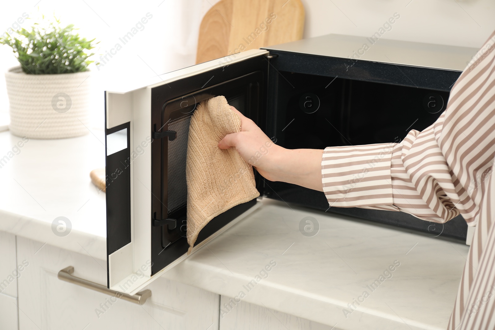 Photo of Woman cleaning microwave oven with rug in kitchen, closeup