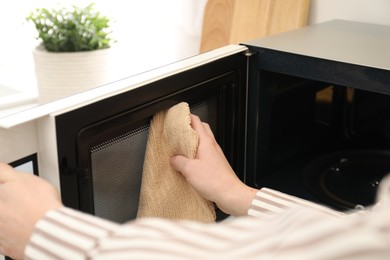 Photo of Woman cleaning microwave oven with rug in kitchen, closeup