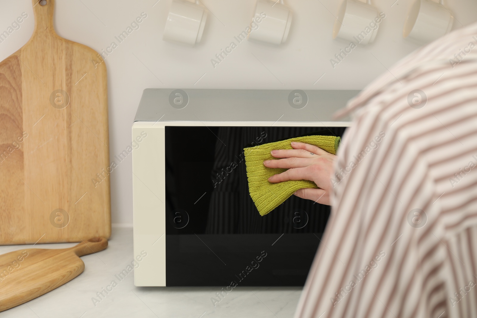 Photo of Woman cleaning microwave oven with rug in kitchen, closeup