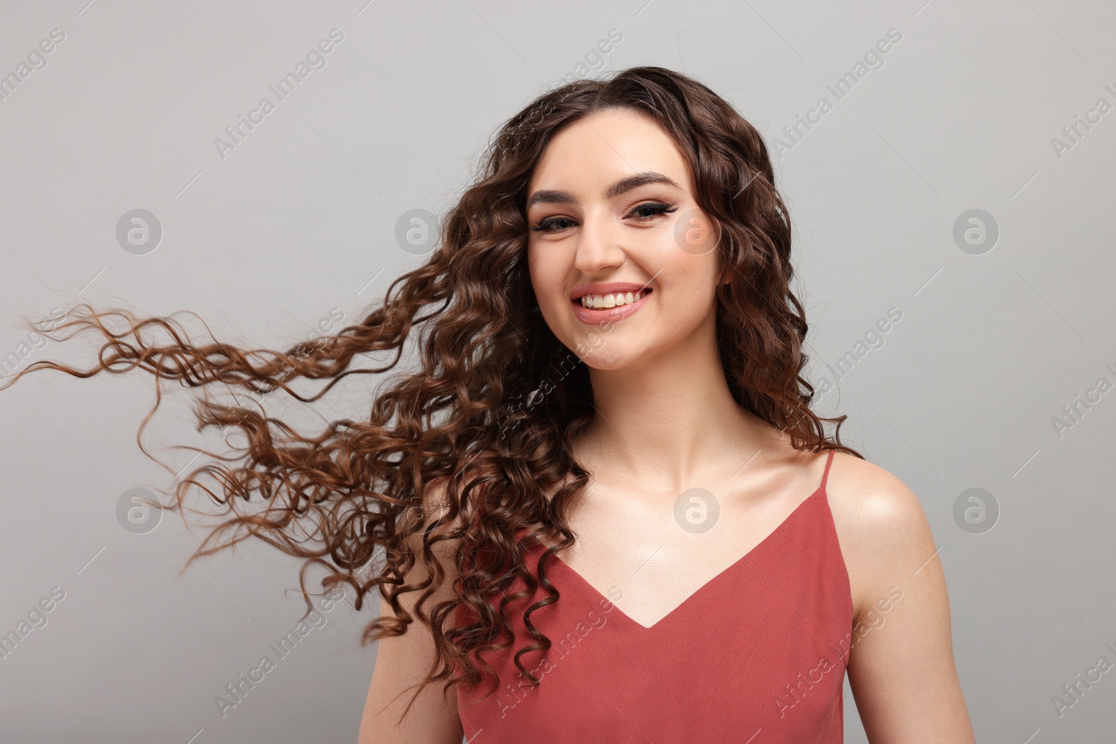 Photo of Beautiful young woman with long curly brown hair on grey background