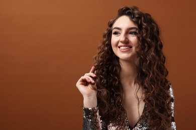 Photo of Beautiful young woman with long curly hair in sequin dress on brown background, space for text