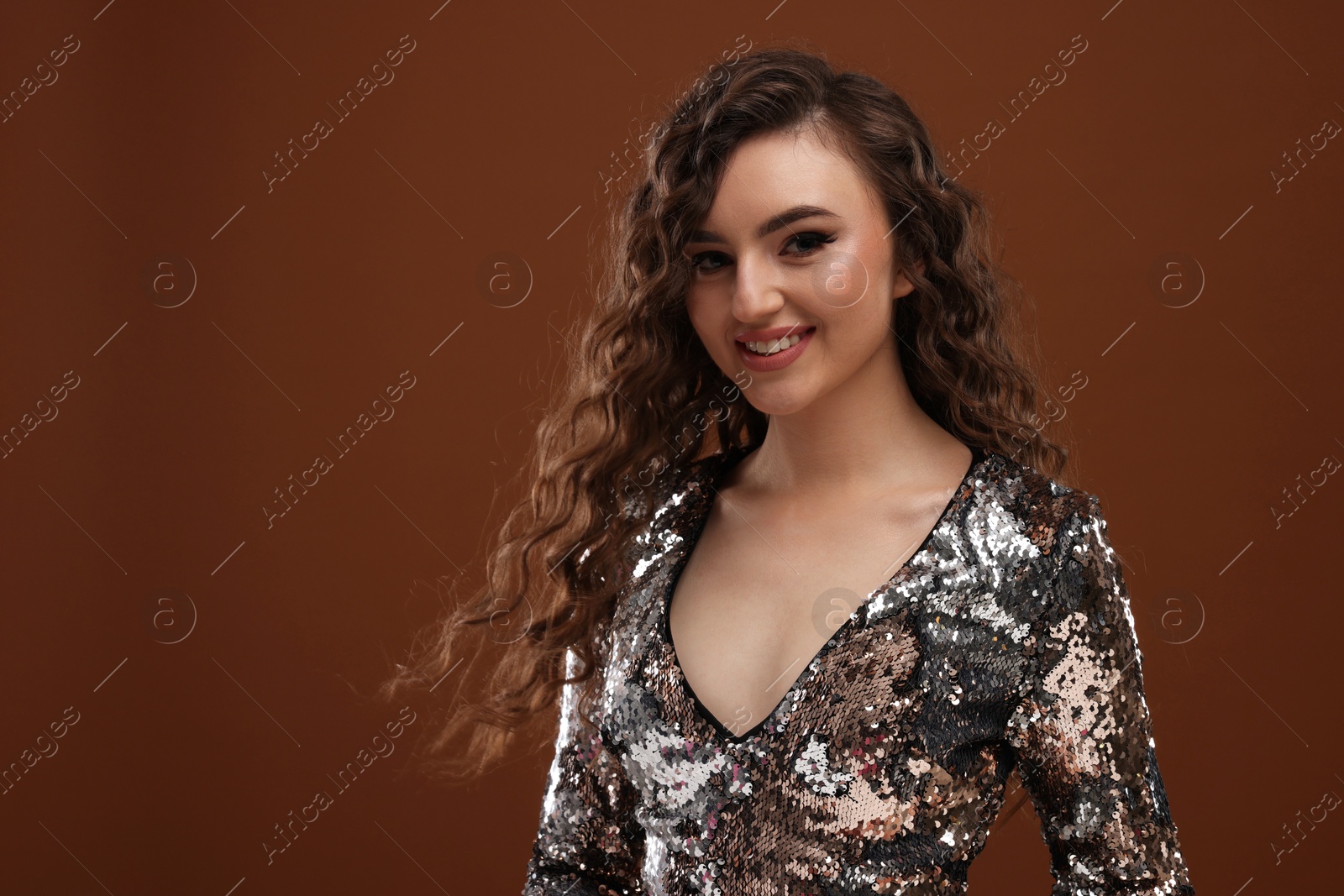 Photo of Beautiful young woman with long curly hair in sequin dress on brown background, space for text