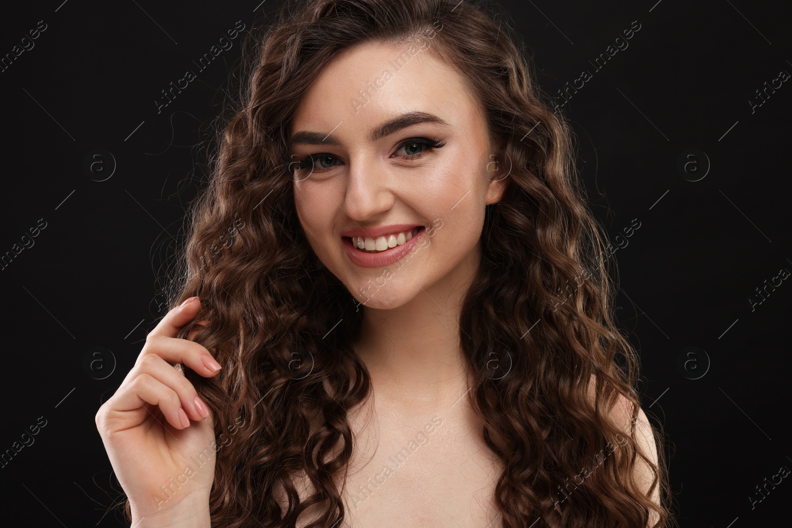 Photo of Beautiful young woman with long curly brown hair on black background