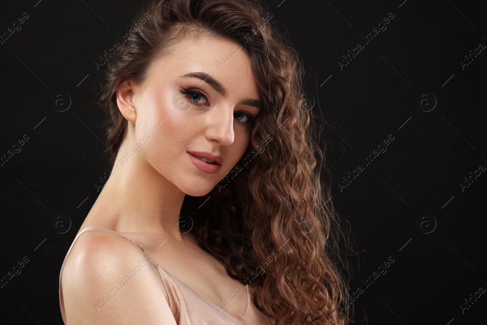 Photo of Beautiful young woman with long curly brown hair on black background, space for text