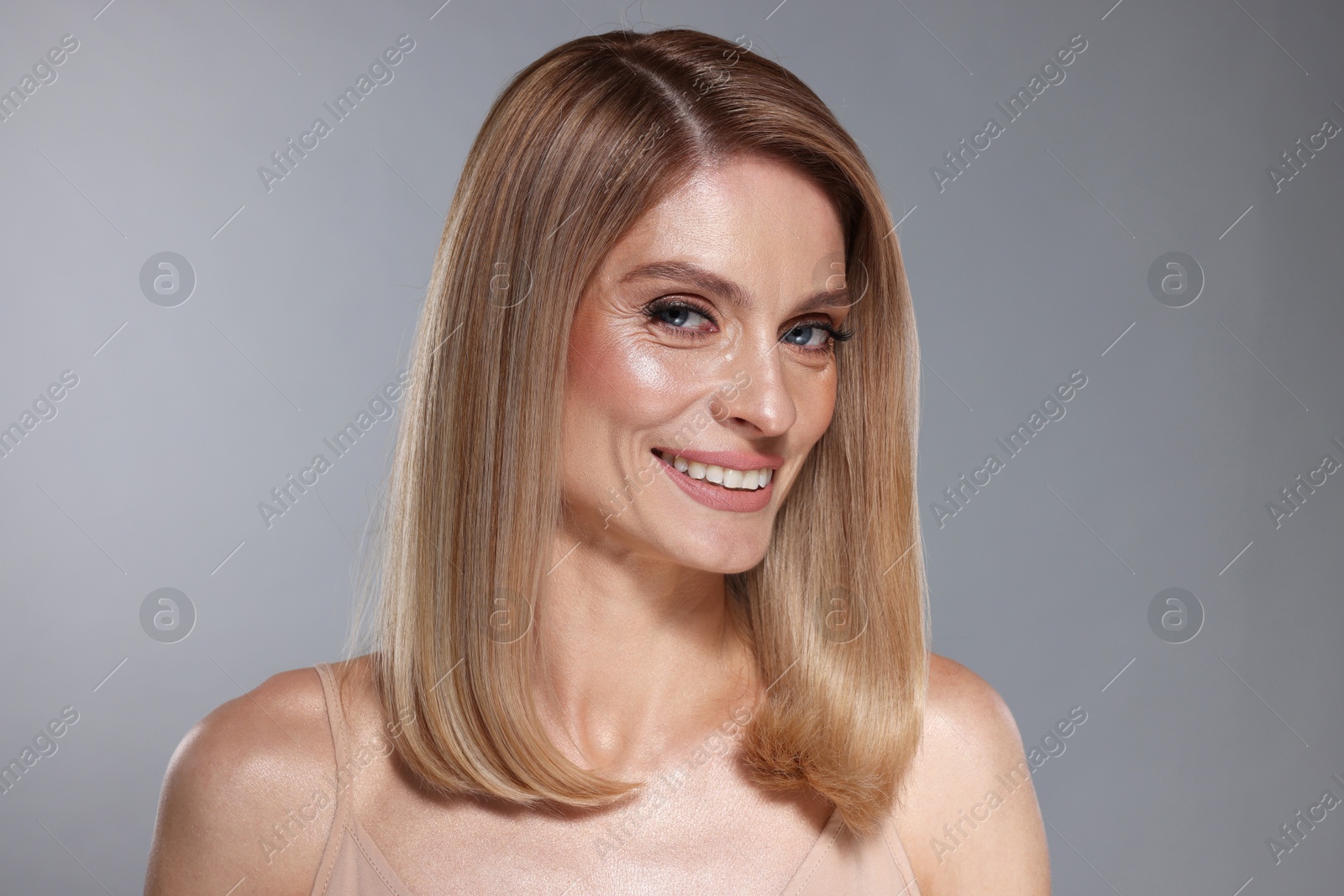 Photo of Portrait of beautiful happy woman with straight blonde hair on grey background