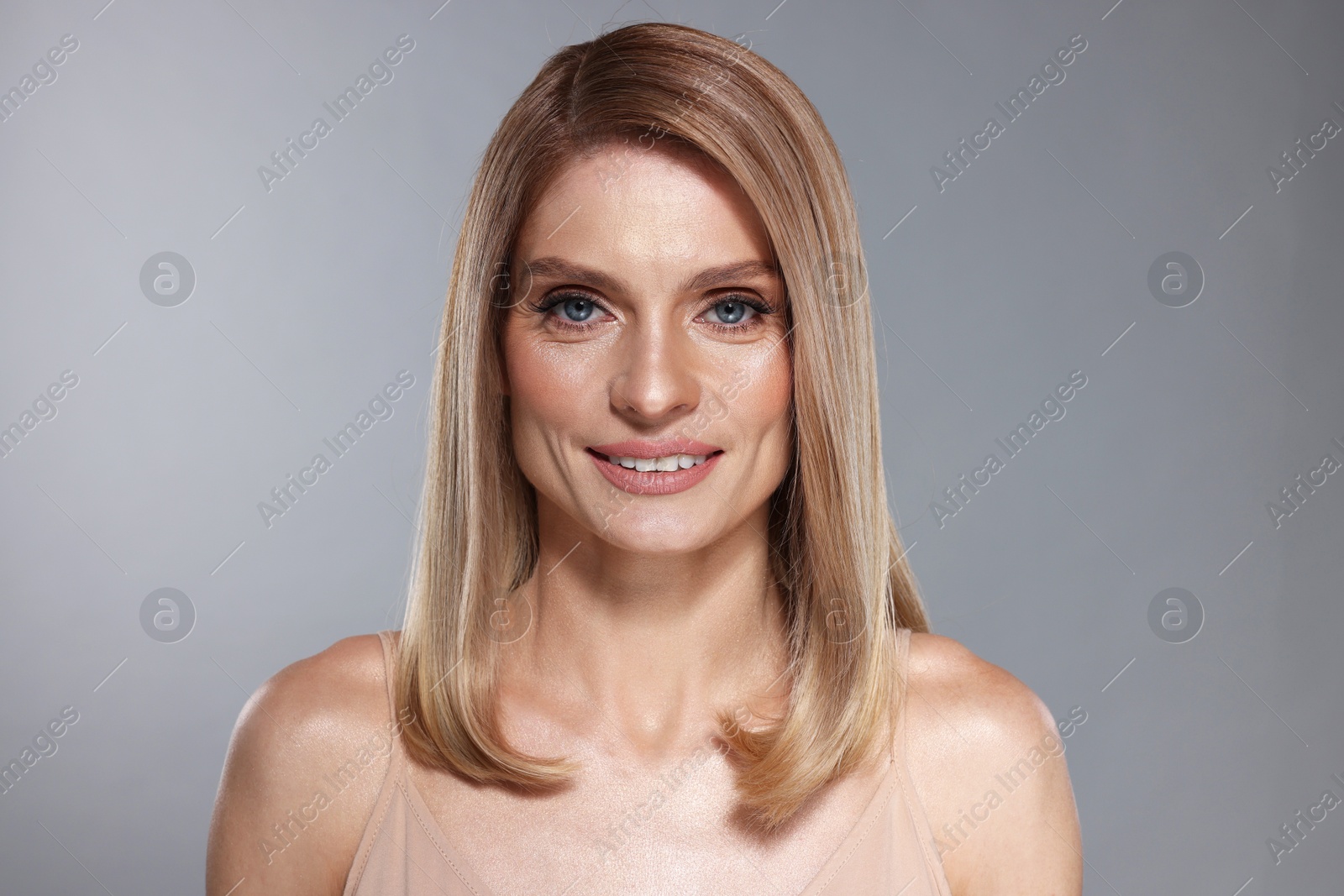 Photo of Portrait of beautiful happy woman with straight blonde hair on grey background