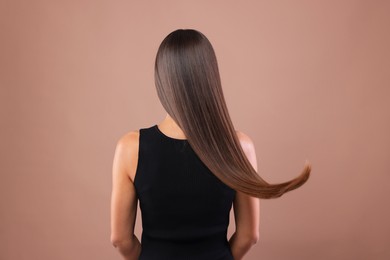 Photo of Hair styling. Woman with straight long hair on pale brown background, back view