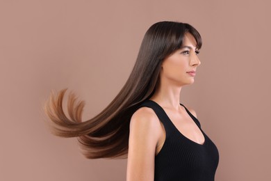 Photo of Hair styling. Beautiful woman with straight long hair on pale brown background