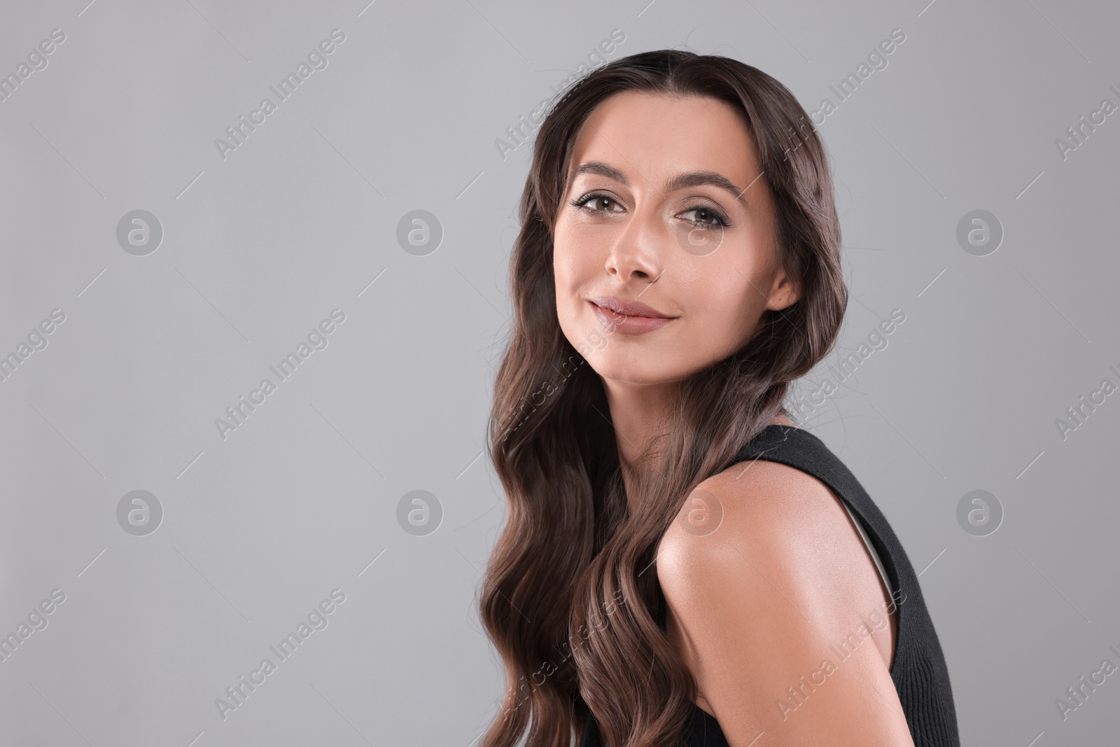 Photo of Hair styling. Portrait of beautiful woman with wavy long hair on grey background. Space for text