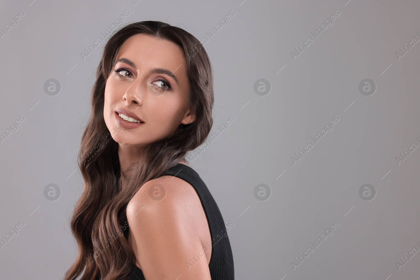 Photo of Hair styling. Beautiful woman with wavy long hair on grey background, space for text