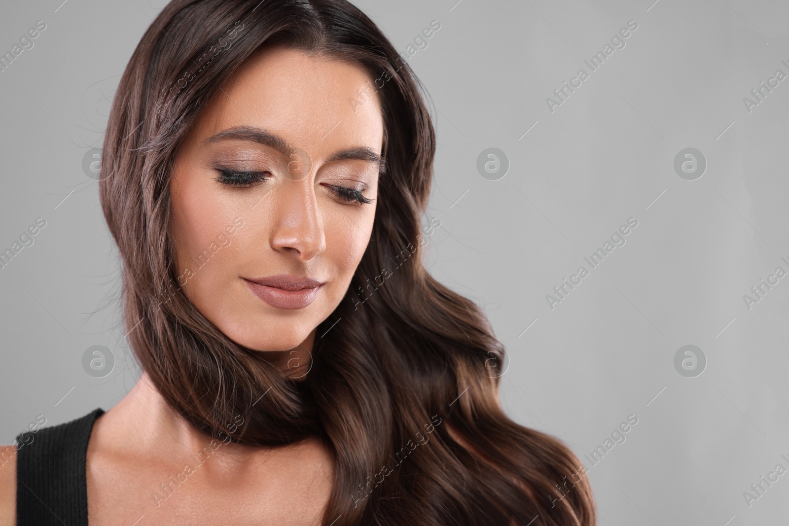 Photo of Hair styling. Beautiful woman with wavy long hair on grey background, closeup. Space for text