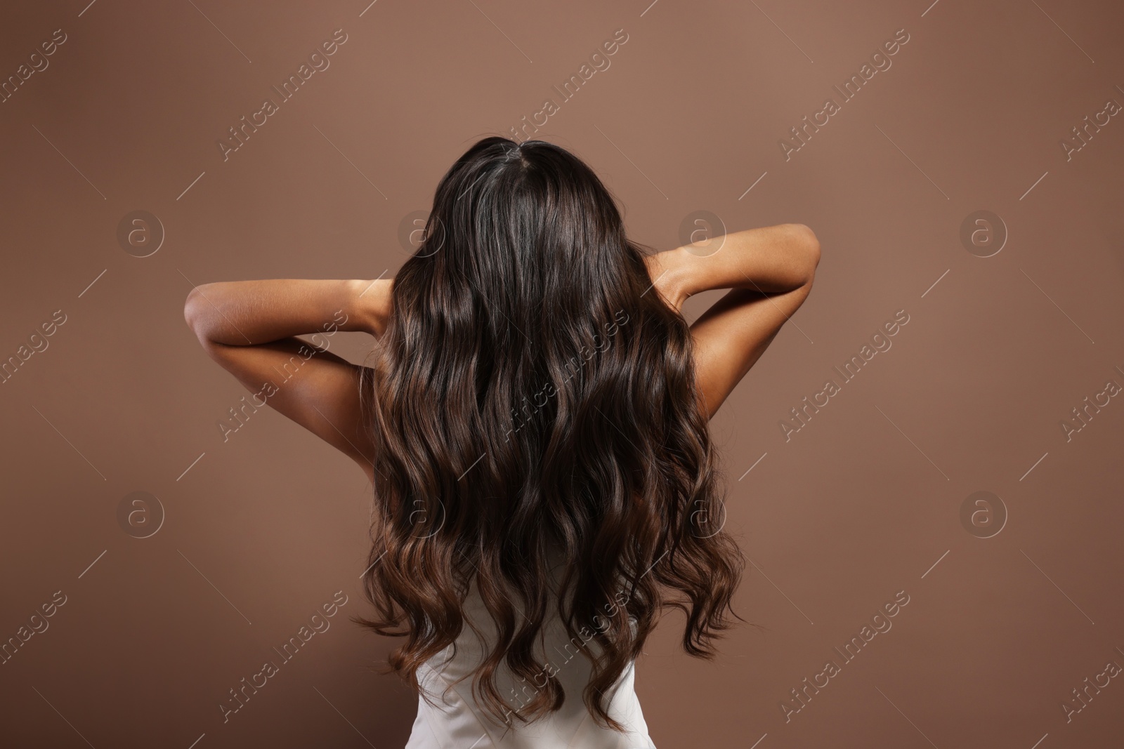 Photo of Hair styling. Woman with wavy long hair on brown background, back view