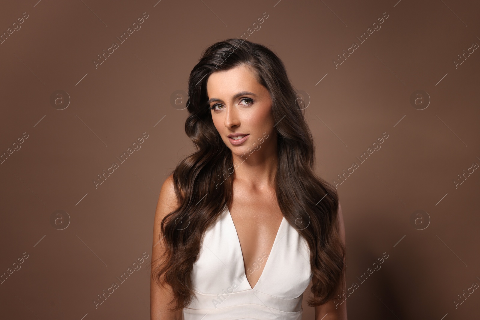 Photo of Hair styling. Portrait of beautiful woman with wavy long hair on brown background