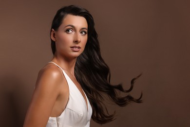 Photo of Hair styling. Beautiful woman with wavy long hair on brown background, space for text