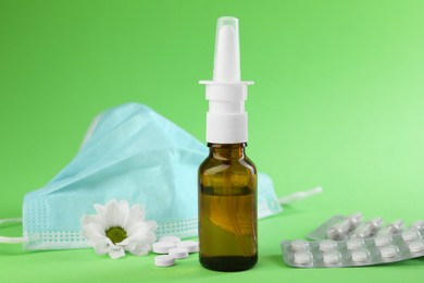 Photo of Allergy treatment. Nasal spray, pills, protective mask and flower on green background