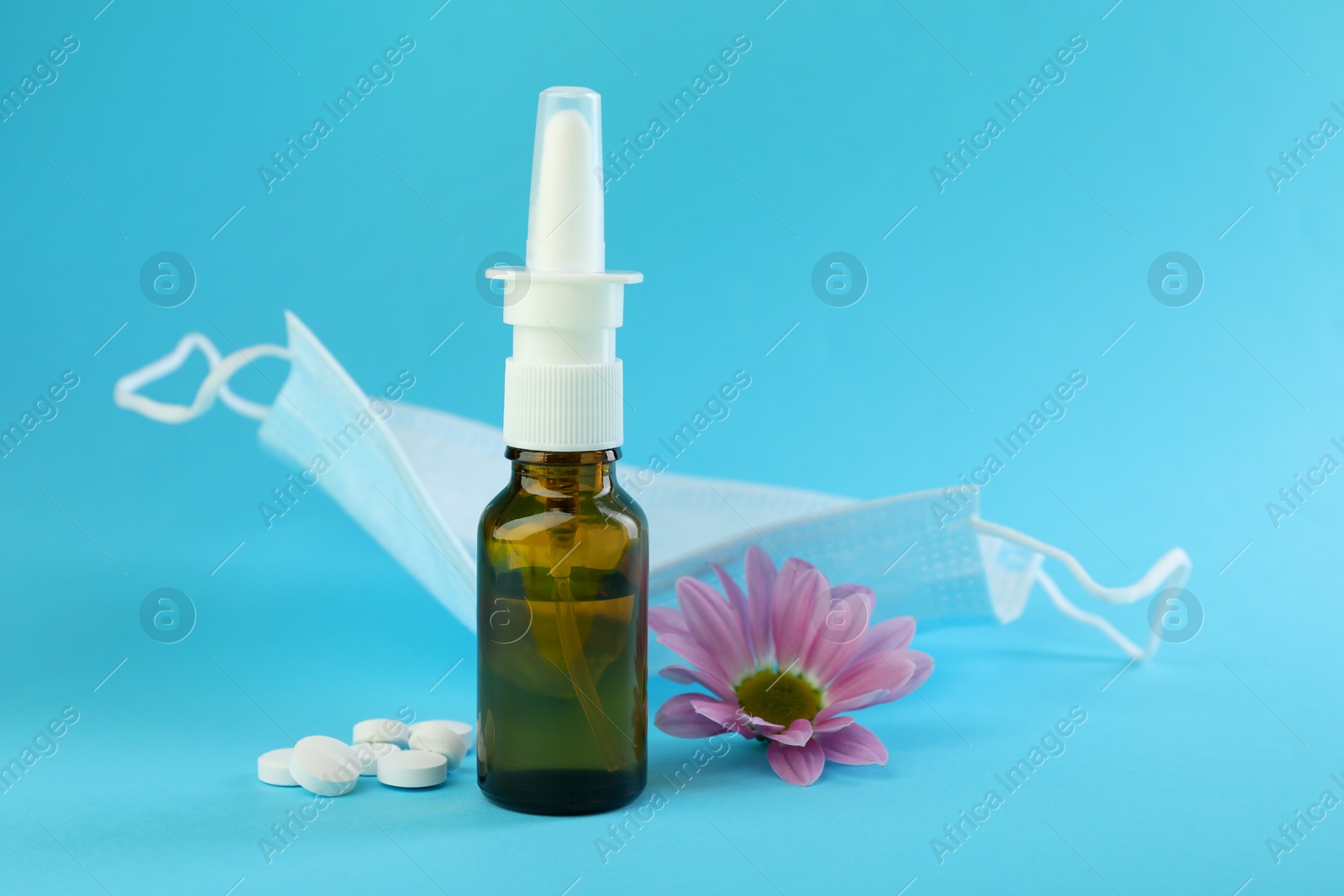 Photo of Allergy treatment. Nasal spray, pills, protective mask and flower on light blue background