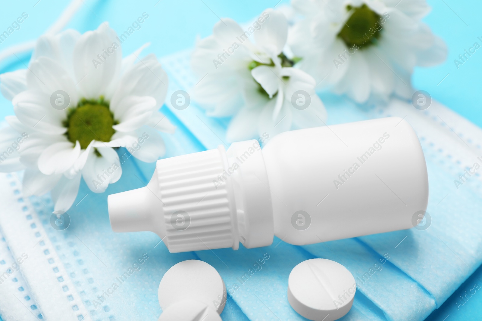 Photo of Allergy treatment. Nasal drops, pills, flowers and protective mask on light blue background, closeup