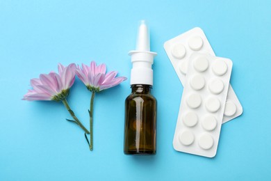 Photo of Allergy treatment. Nasal spray, pills and flowers on light blue background, flat lay