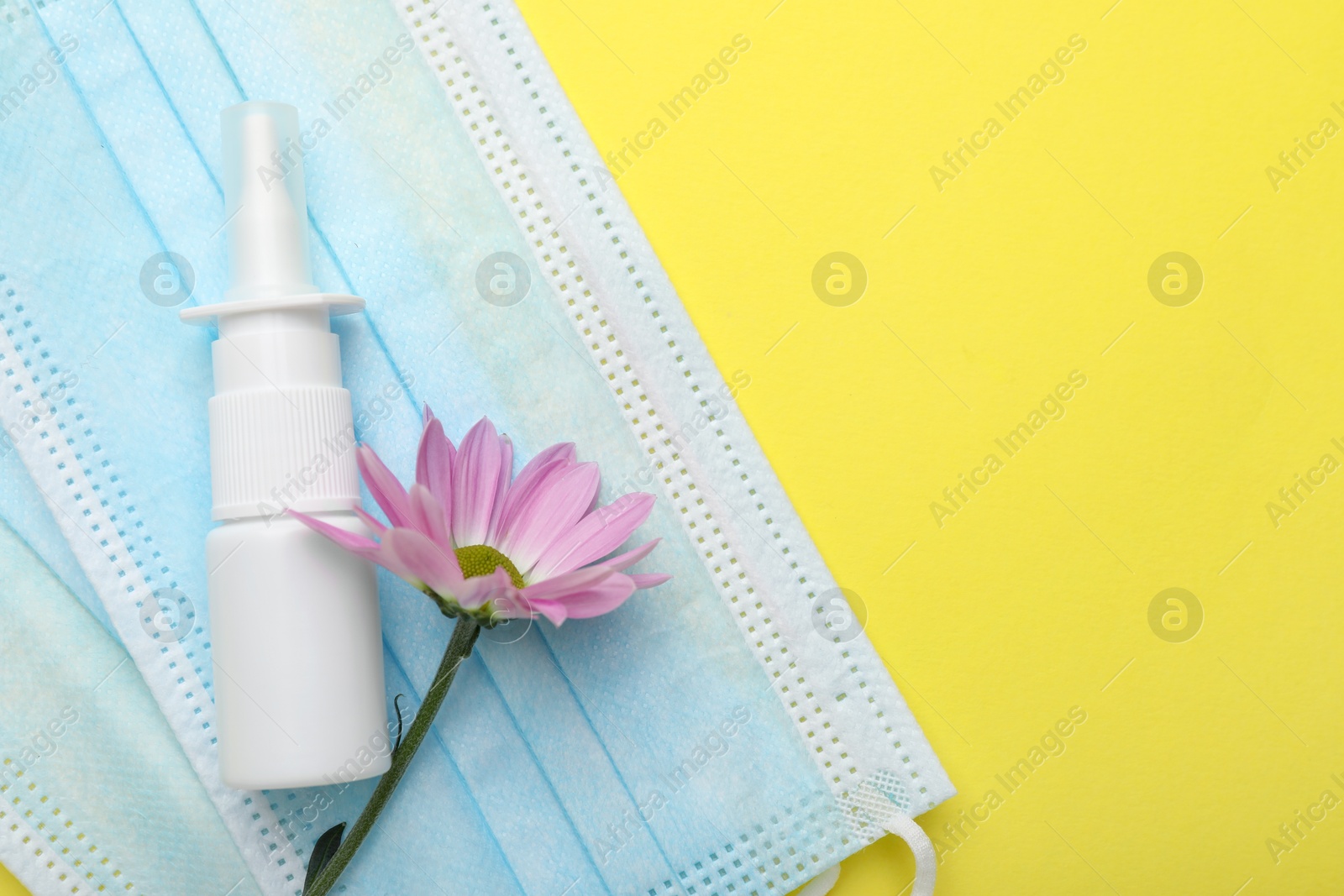 Photo of Allergy treatment. Nasal spray, protective masks and flower on yellow background, top view. Space for text