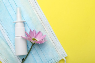 Photo of Allergy treatment. Nasal spray, protective masks and flower on yellow background, top view. Space for text