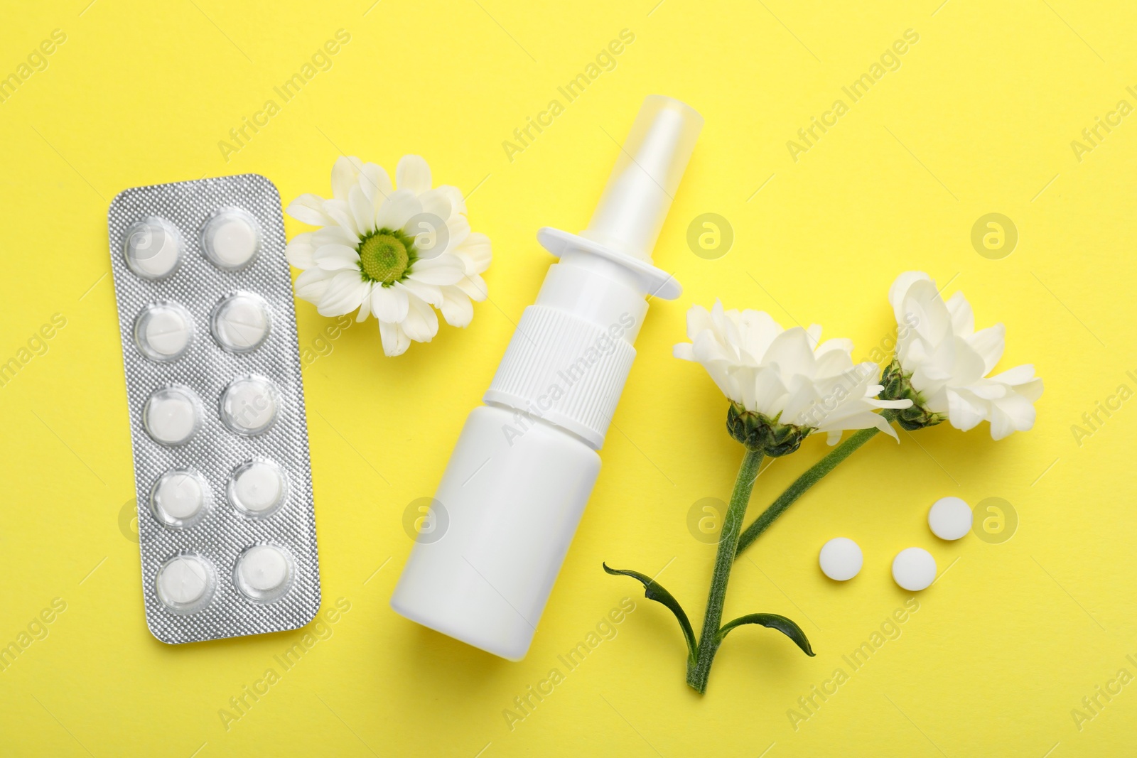 Photo of Allergy treatment. Nasal spray, pills and flowers on yellow background, flat lay