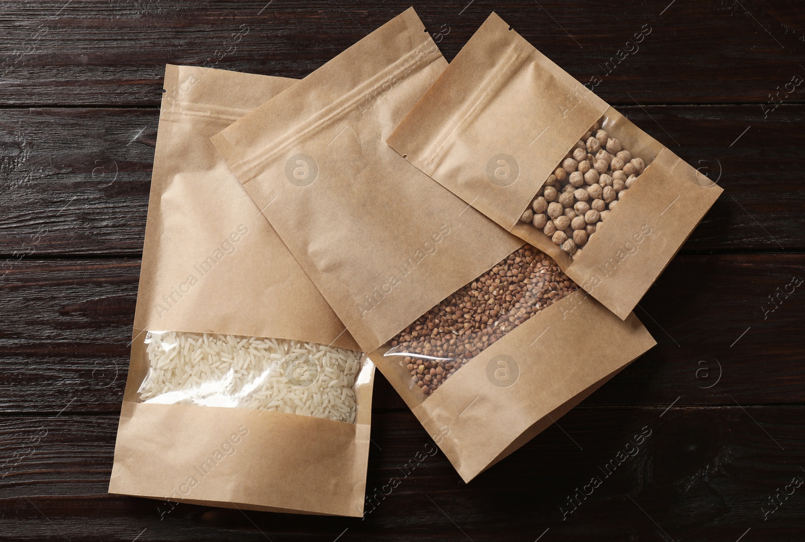 Photo of Paper pouch bags with buckwheat, chickpeas and rice on wooden table, flat lay