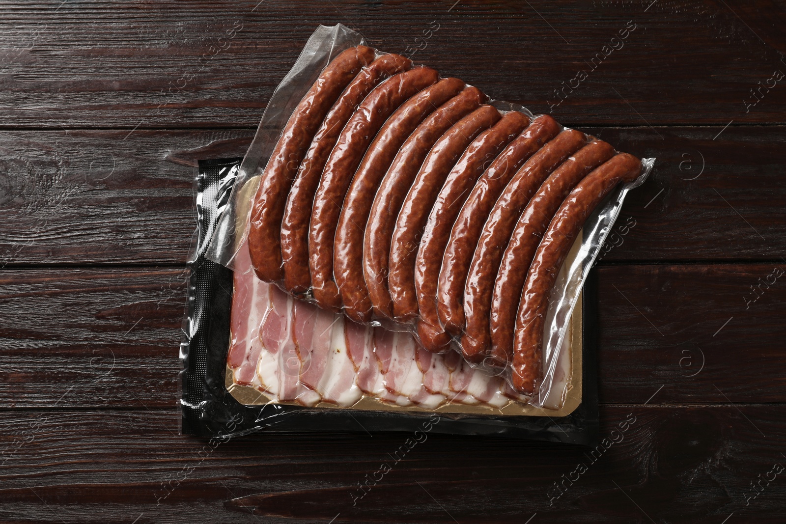 Photo of Packs of dry smoked sausages and sliced bacon on wooden table, top view