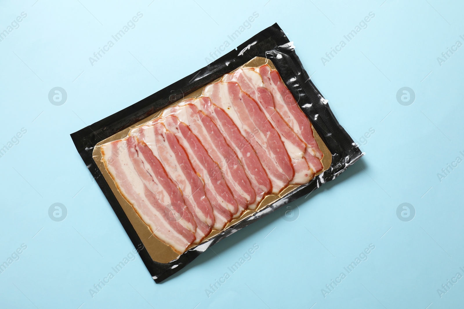 Photo of Pack of bacon on light blue background, top view