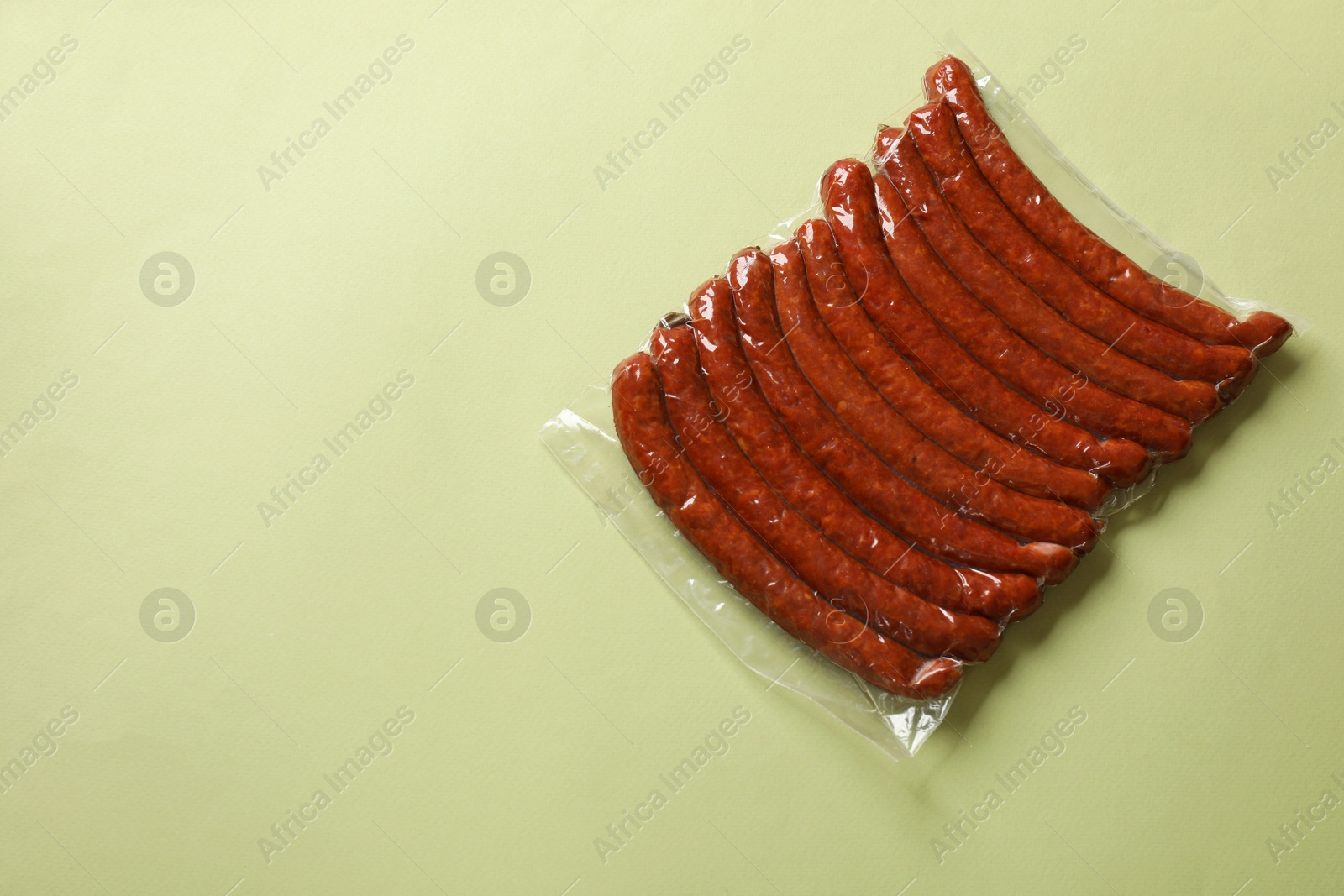 Photo of Pack of smoked sausages on green background, top view. Space for text