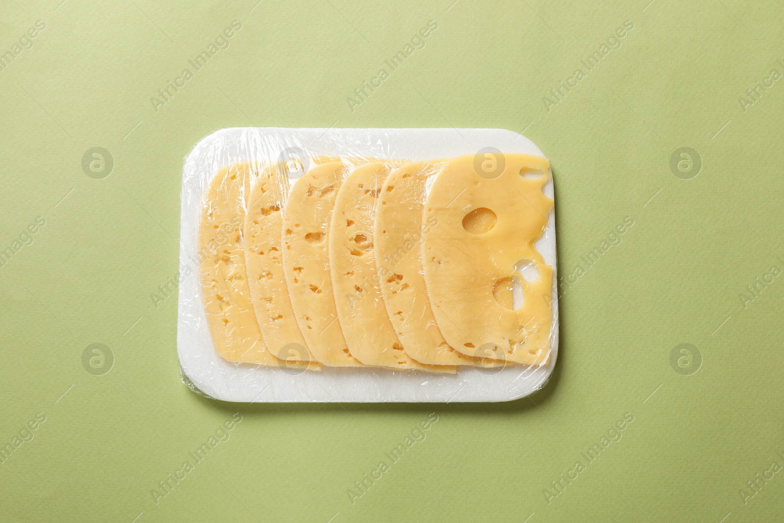 Photo of Pack of sliced cheese on green background, top view