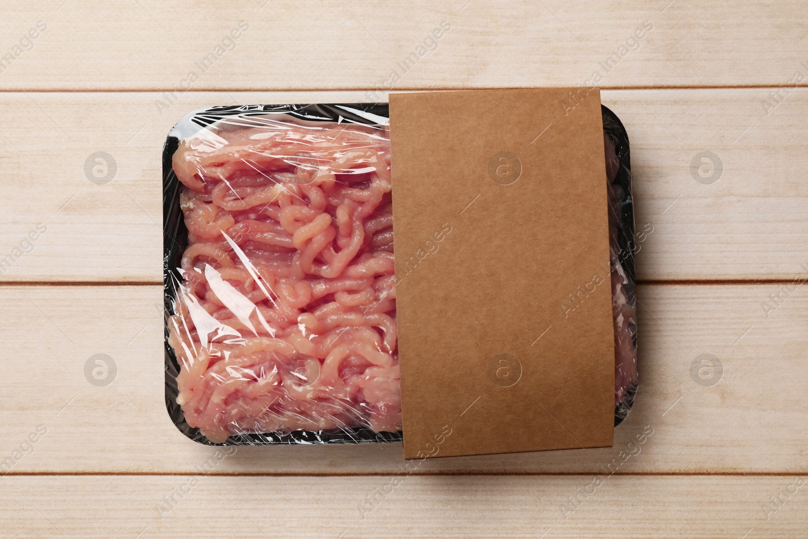 Photo of Plastic pack with fresh minced meat on light wooden table, top view