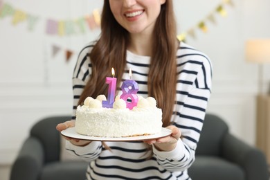 Photo of Coming of age party - 18th birthday. Happy young woman holding tasty cake with number shaped candles at home, closeup