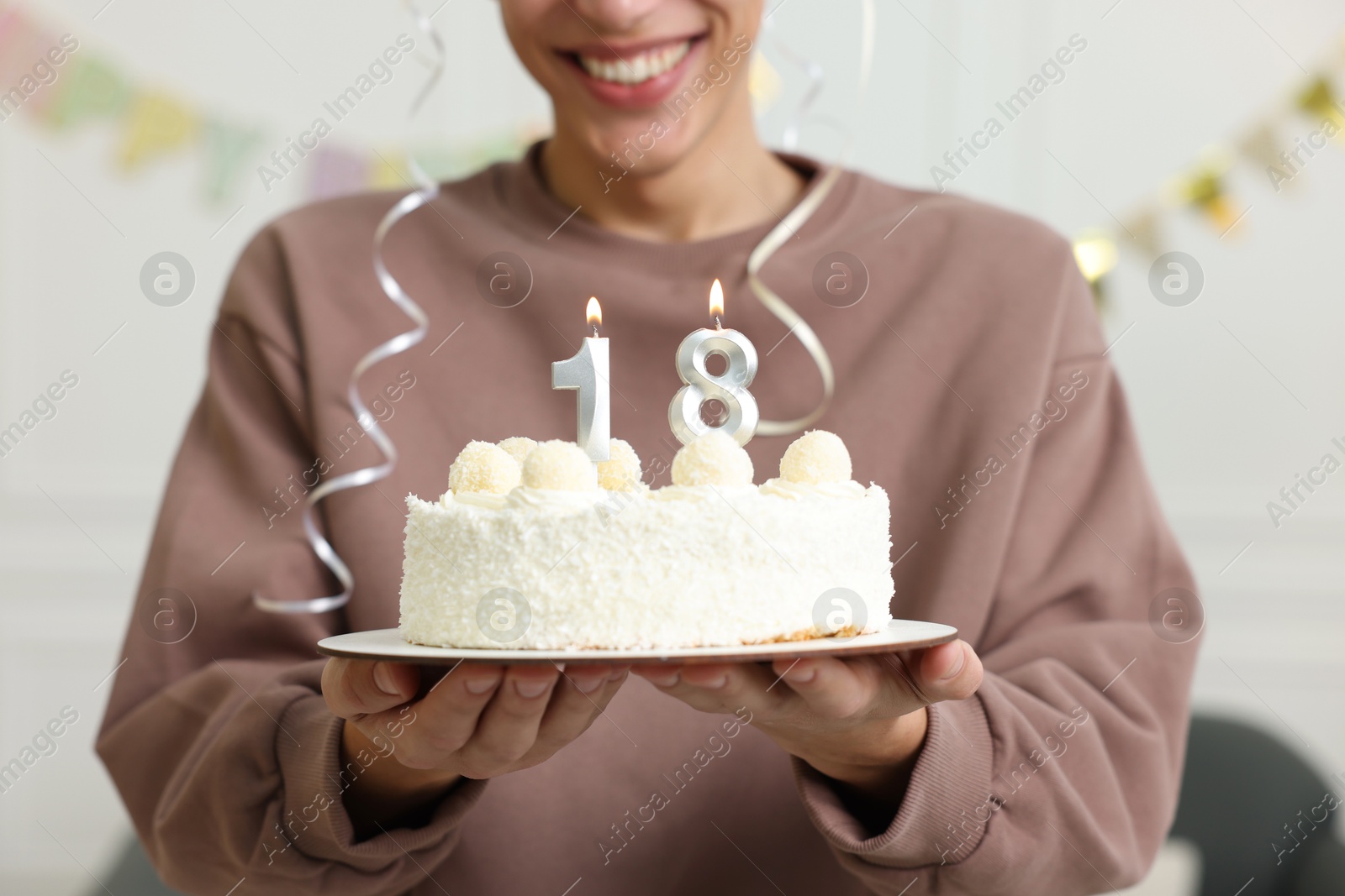 Photo of Coming of age party - 18th birthday. Happy young man holding tasty cake with number shaped candles at home, closeup