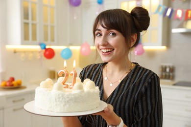 Photo of Coming of age party - 21st birthday. Happy young woman holding tasty cake with number shaped candles at home