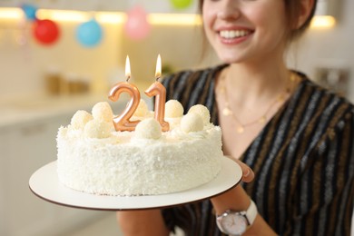 Photo of Coming of age party - 21st birthday. Happy young woman holding tasty cake with number shaped candles at home, closeup