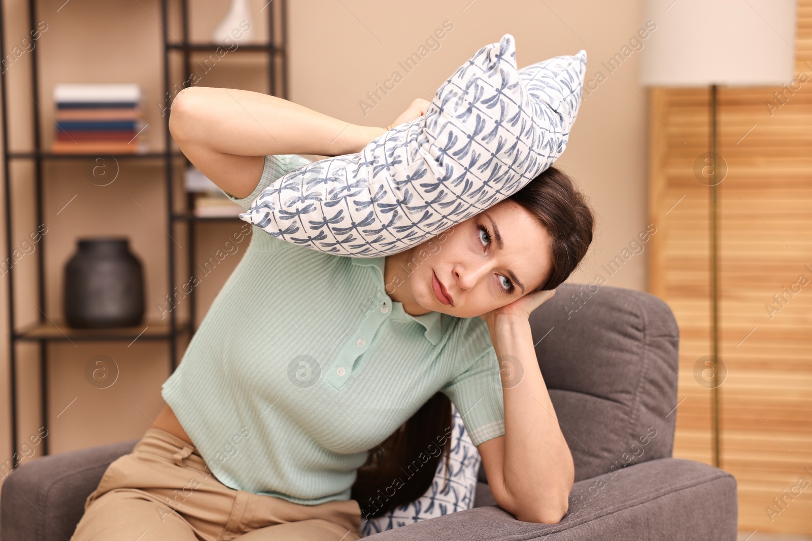 Photo of Annoyed woman covering her ears with pillow due to sound at home