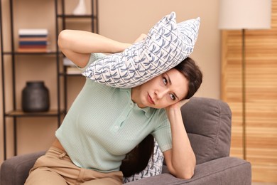 Photo of Annoyed woman covering her ears with pillow due to sound at home