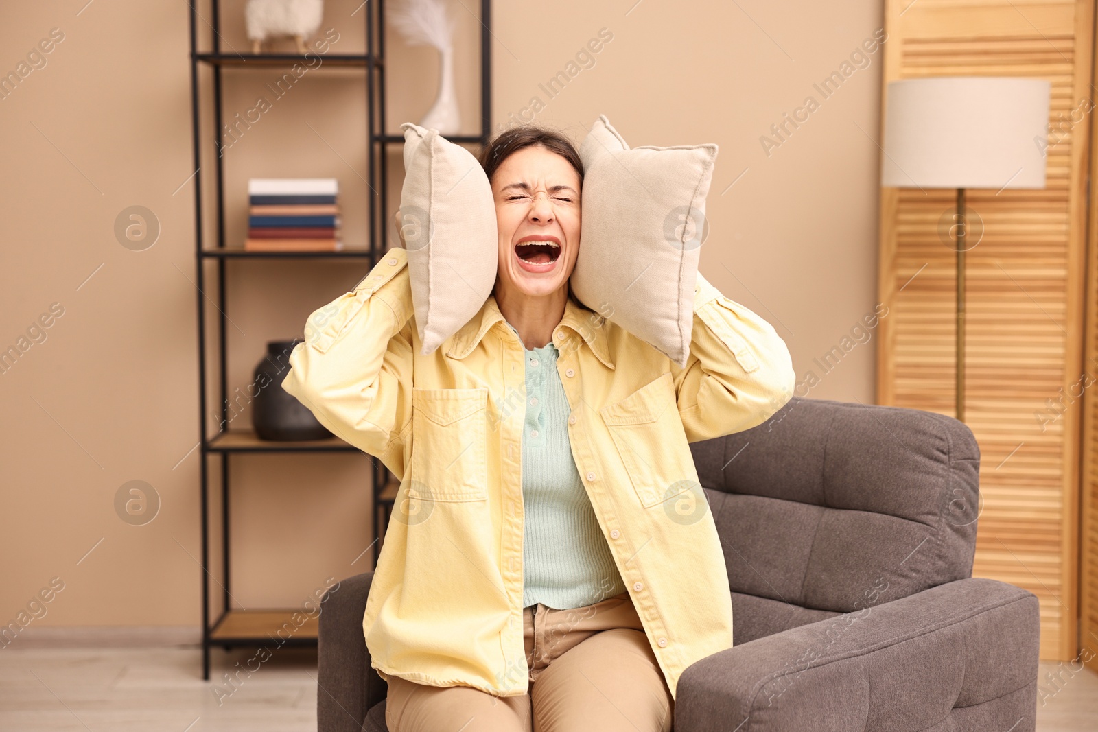 Photo of Annoyed woman covering her ears with pillows due to loud sound at home