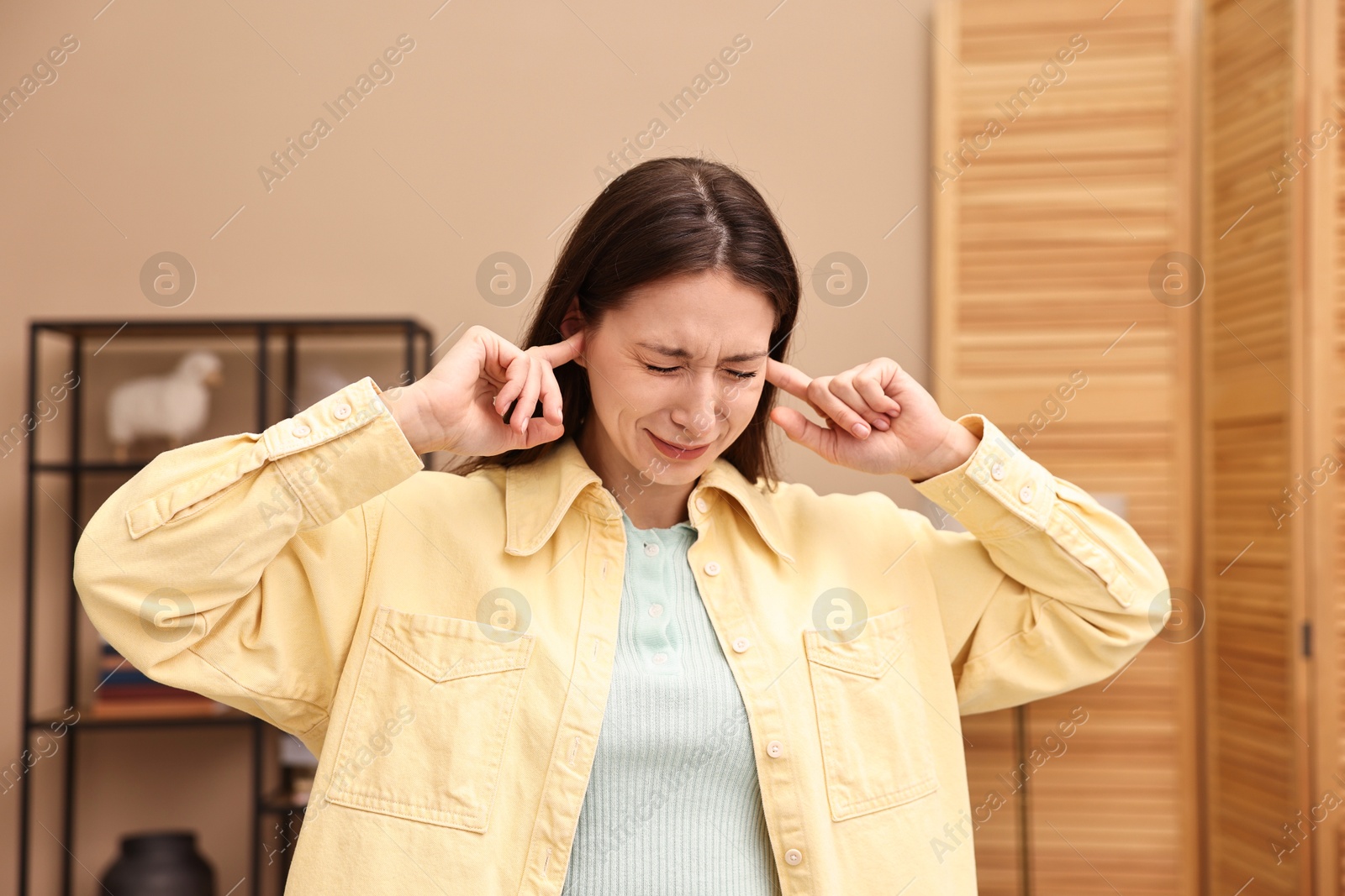 Photo of Annoyed woman covering her ears due to loud sound at home